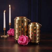 Two metallic lanterns with decorative elements on a wooden surface with pink flowers and candles.